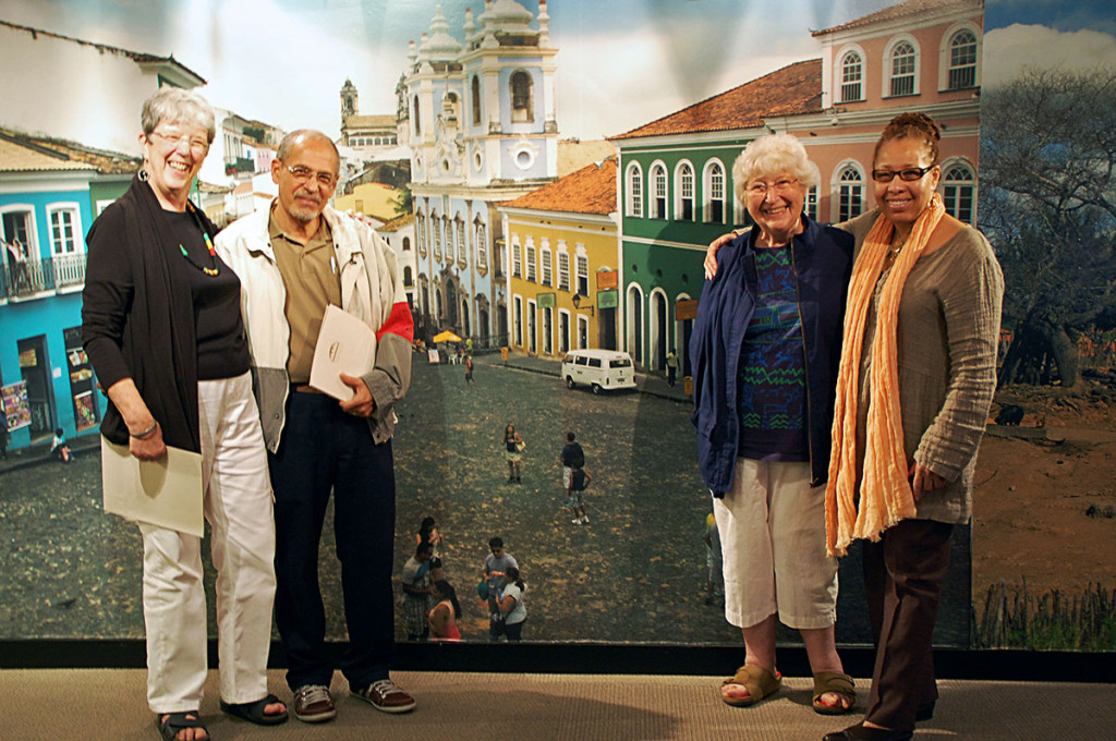 PICTURED HERE: Mame Jackson and Barb Cervenka are joined by Antônio Neto, photographer from Salvador, Bahia and Juanita Moore, President and CEO of the Wright Museum, in front of a photo-mural of the Pelourinho, taken by Antônio Neto for the entrance of the exhibition.
